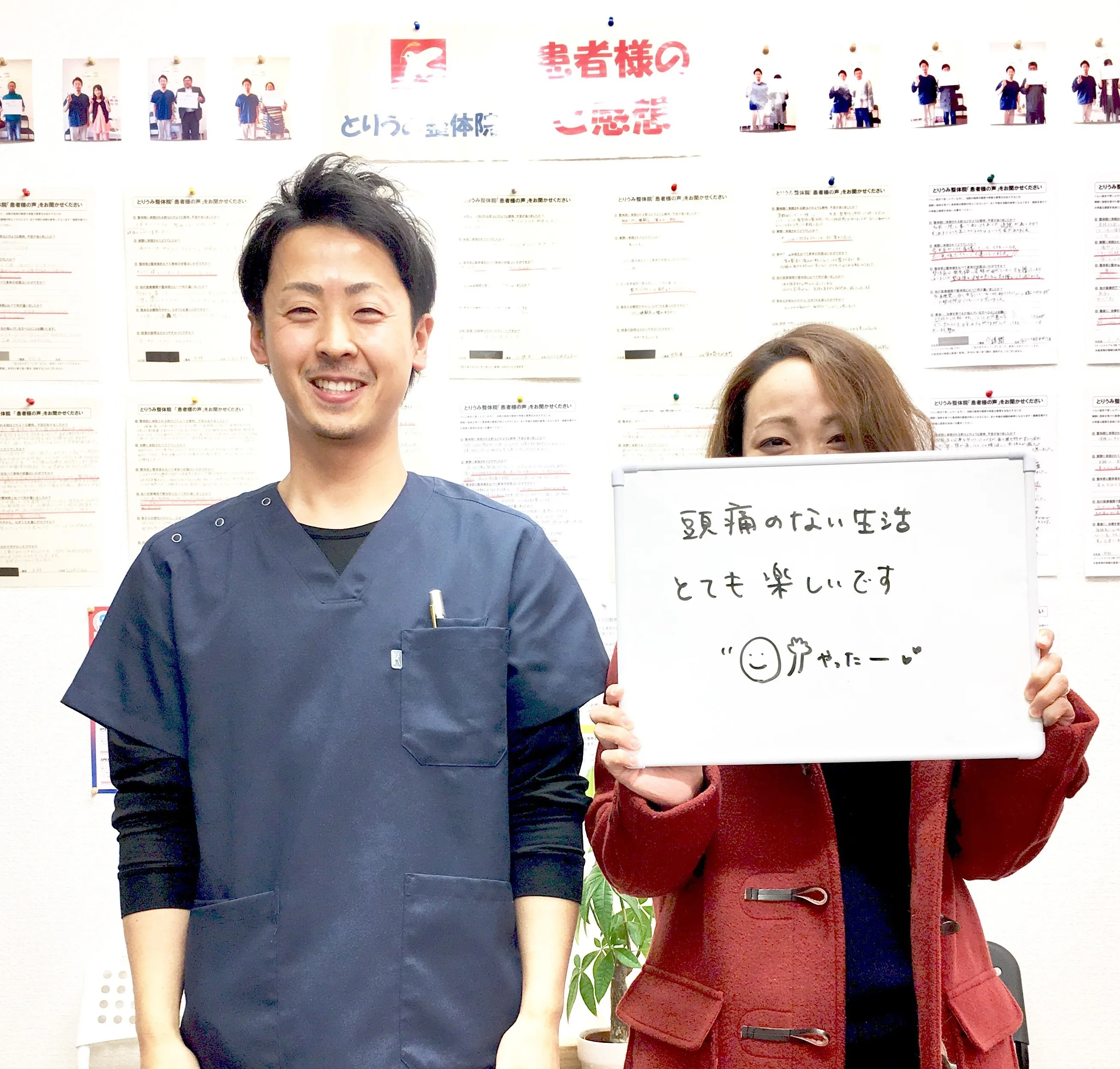 とりうみ整体院の院長と患者様の写真。ホワイトボードに「頭痛のない生活 とても楽しいです」と書かれている